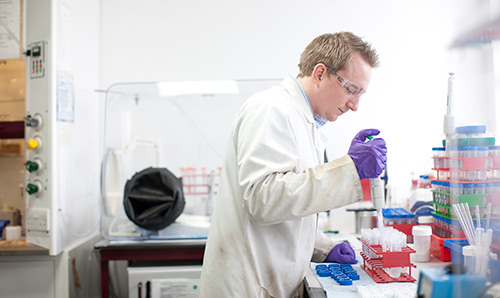Lab coat-wearing male student squeezing pipette into test tube