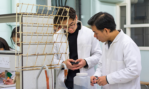 Two male researchers in lab coats looking at information on a mobile phone