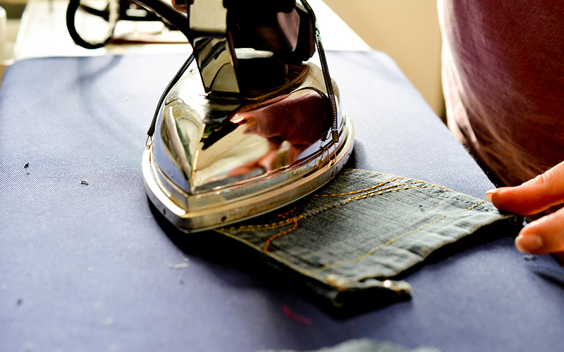 A metal iron being used on a patch of denim
