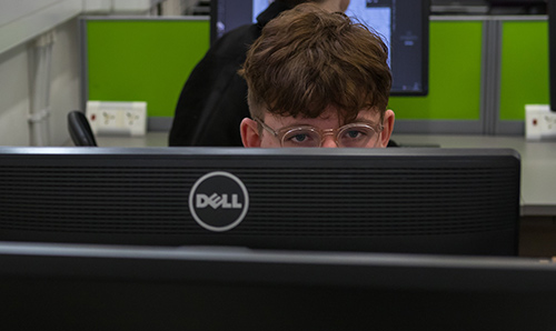 Male student with glasses reading his computer screen