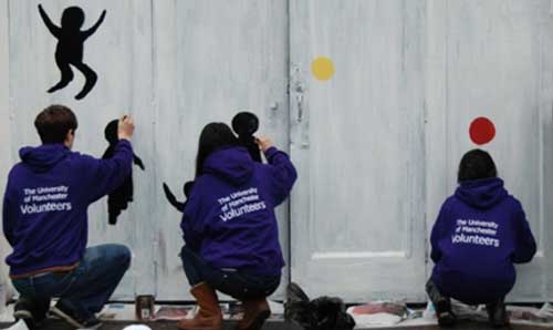 Three student volunteers creating art on a set of large doors.