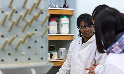 A female student in a lab coat discussing her work with others